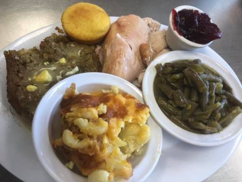 A plate of comfort food featuring cornbread, turkey, green beans, macaroni and cheese, stuffing, and cranberry sauce.