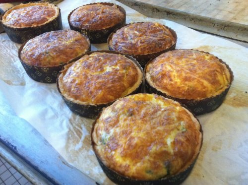 Freshly baked savory muffins in black paper liners, golden brown and fluffy, arranged on a baking tray.