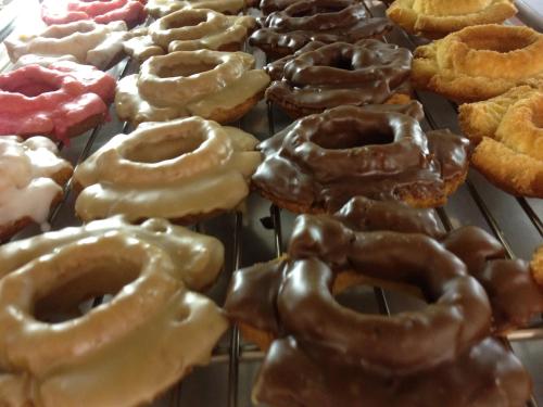 A variety of donuts on a cooling rack, featuring chocolate, glazed, and cream toppings.