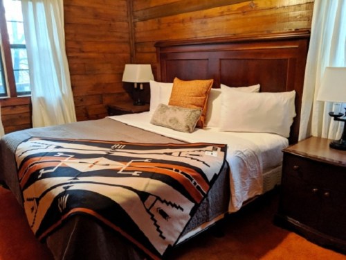 Cozy bedroom with a wooden interior, featuring a large bed, decorative blanket, and bedside lamps.