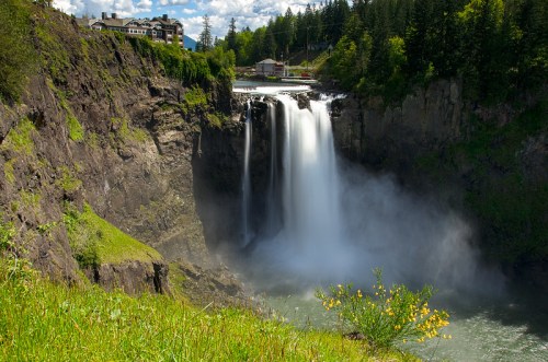 A scenic view of a waterfall cascading down rocky cliffs, surrounded by lush greenery and a clear blue sky.
