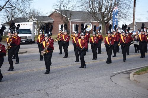 A marching band in uniforms with plumes parades down a street, playing instruments and showcasing their formation.