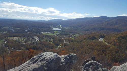 A panoramic view of a valley with autumn foliage, a river, and distant mountains under a clear blue sky.