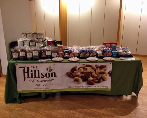 A display table featuring various nut products and snacks from Hillson Nut Company, with packaging and samples.