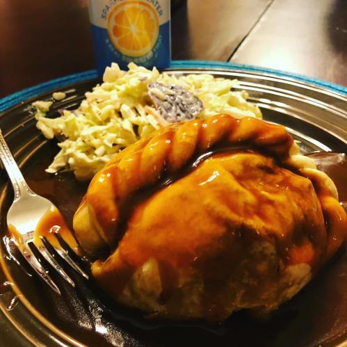 A plate with a saucy dish, coleslaw, and a can of soda on the side, set on a wooden table.