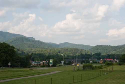 A scenic view of rolling green hills under a cloudy sky, with a small town visible in the foreground.