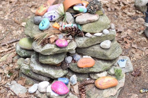 A stacked arrangement of rocks and painted stones, adorned with pinecones and small natural elements, in a forest setting.