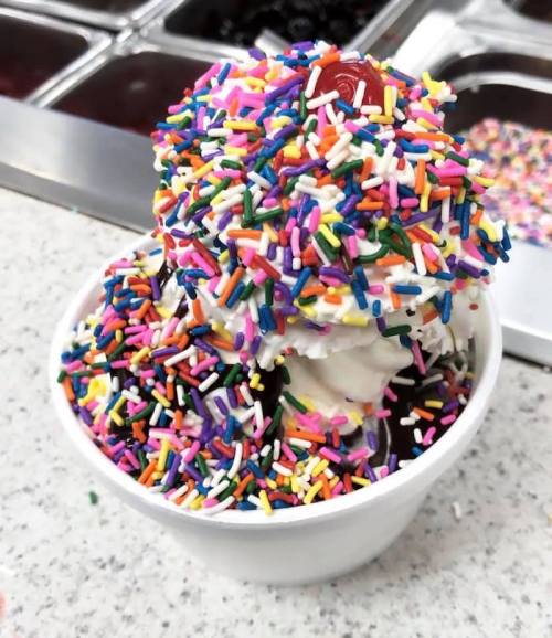 A cup of ice cream topped with colorful sprinkles and a cherry.