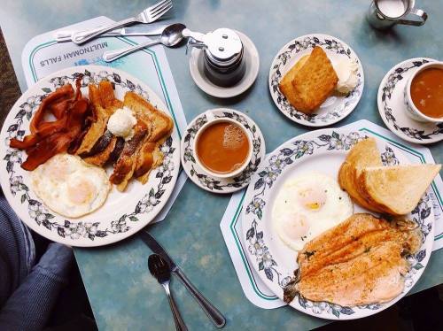 A table set with two plates of breakfast: bacon, eggs, toast, and coffee, all on floral-patterned dishes.