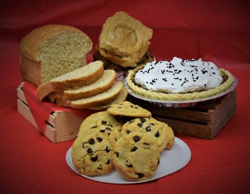 A variety of baked goods: sliced bread, a pie with whipped cream, and chocolate chip cookies on a plate, against a red background.