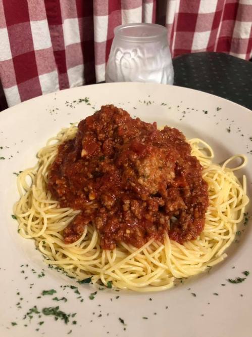 A plate of spaghetti topped with meat sauce and herbs, set on a checkered tablecloth with a candle in the background.