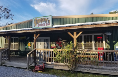 A green building with a wooden porch, featuring a sign that reads "Dempsey's Seafood & Grill" and an open sign in the window.