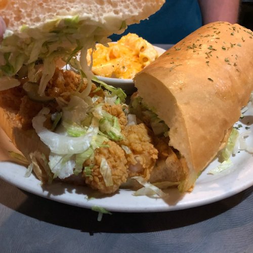 A close-up of a sandwich filled with fried shrimp and lettuce, served with a side of macaroni and cheese.