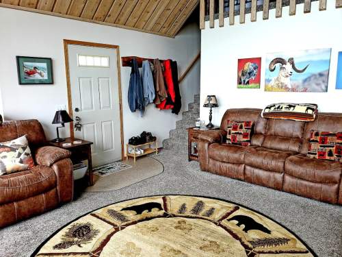 Cozy living room with brown leather sofas, a round rug, and a welcoming entryway with coats and artwork on the walls.
