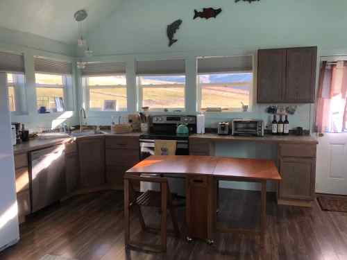 Bright kitchen with light blue walls, wooden cabinets, and a small table, featuring appliances and a scenic view outside.
