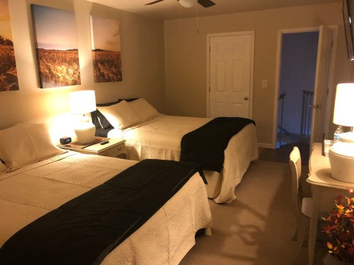 Cozy hotel room with two beds, bedside lamps, and artwork on the walls, featuring a warm color palette.