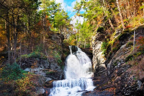 A serene waterfall cascading down rocky cliffs, surrounded by lush green trees and autumn foliage.
