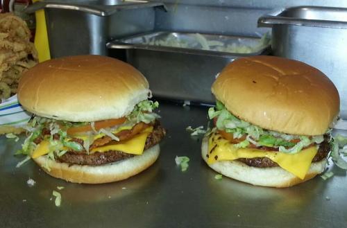 Two cheeseburgers with lettuce, tomato, and cheese on soft buns, placed on a metal countertop.
