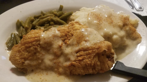 A plate of fried chicken with gravy, mashed potatoes, and green beans.