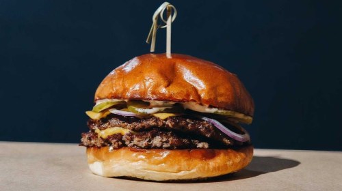 A juicy burger with two patties, cheese, pickles, onions, and a toasted bun, held together with a toothpick.
