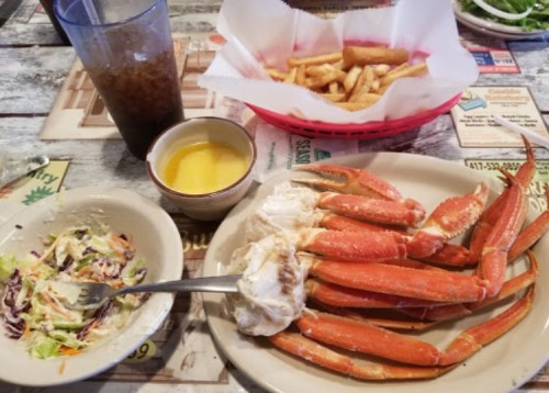 A plate of crab legs with melted butter, a side salad, and a basket of fries, alongside a glass of iced tea.