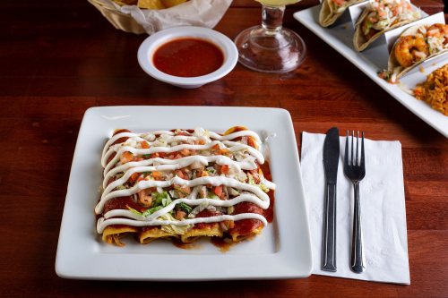 A plate of enchiladas topped with shrimp, lettuce, and sour cream, served with salsa on a wooden table.
