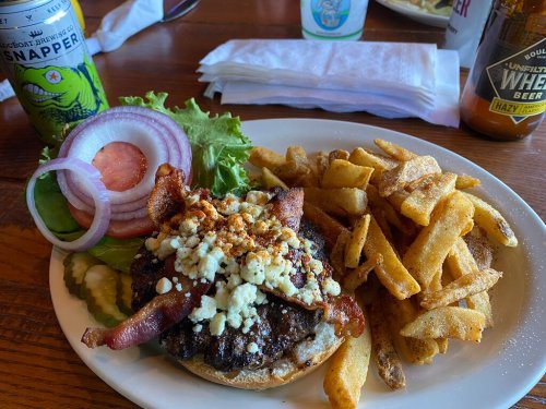 A burger topped with bacon and blue cheese, served with fries and a drink on a wooden table.