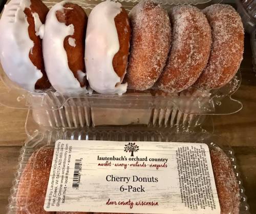 A clear plastic container holding a 6-pack of cherry donuts, some topped with white icing and others with sugar.