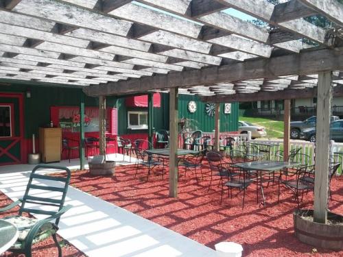 Outdoor dining area with wooden pergola, tables, and chairs on red mulch, next to a green building.