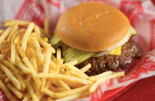 A cheeseburger with pickles and a side of golden French fries in a red basket.