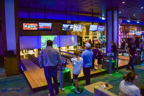 A vibrant bowling alley with multiple lanes, screens, and people enjoying games and activities.