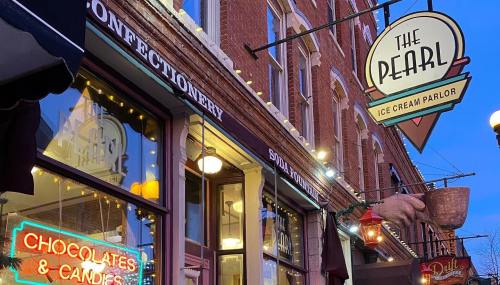 A charming storefront featuring "The Pearl Ice Cream Parlor" sign and a neon "Chocolates & Candies" display.