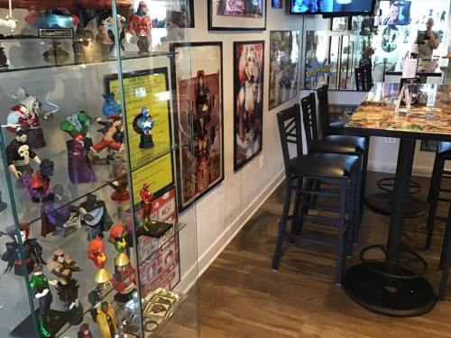 A cozy bar area featuring a display of colorful figurines, framed posters, and seating along the wall.