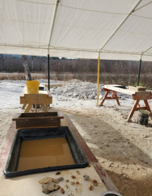 A covered outdoor area with tables, water, and tools for sorting rocks and minerals, surrounded by a natural landscape.