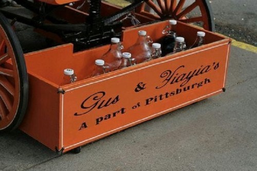 An orange cart with the text "Gus & Tiagui's A part of Pittsburgh" and bottles inside.