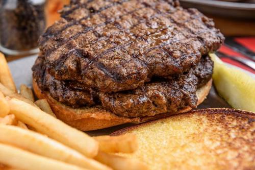 A juicy double burger with grilled patties on a bun, served with crispy French fries and a pickle slice.