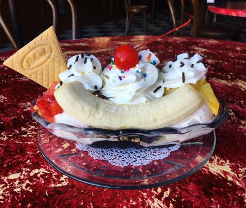 A colorful ice cream sundae topped with whipped cream, cherries, sprinkles, a banana, and a wafer cookie in a glass dish.