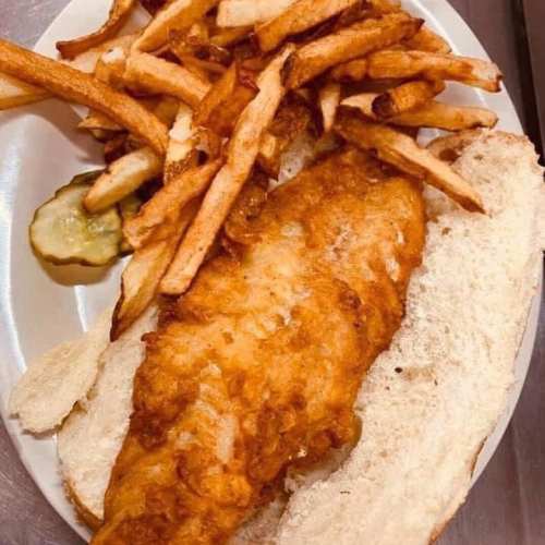 A plate with a fried fish fillet, two slices of bread, French fries, and a pickle slice.