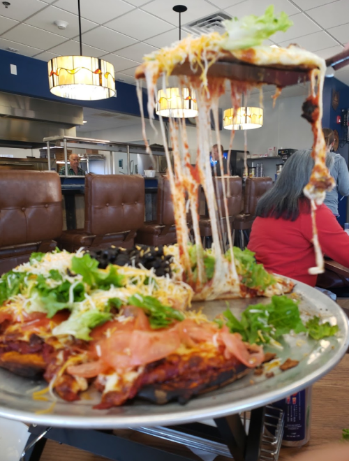 A large pizza topped with lettuce, tomatoes, and cheese, with a slice being lifted, showcasing melted cheese.
