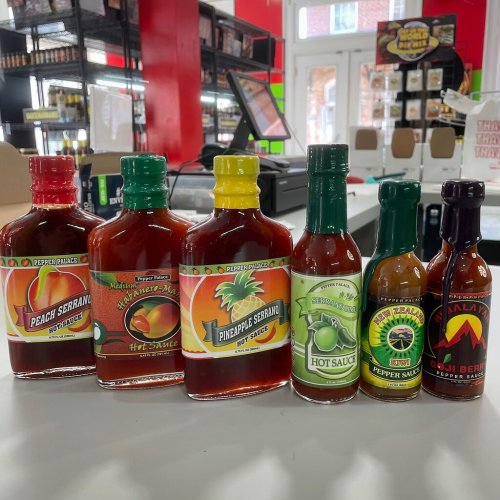 A variety of colorful hot sauces displayed on a shelf, featuring different flavors and bottle designs.