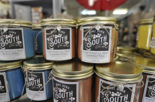 A display of colorful soy candles in jars, labeled with "Hand Poured Soy Blend" and various scents.