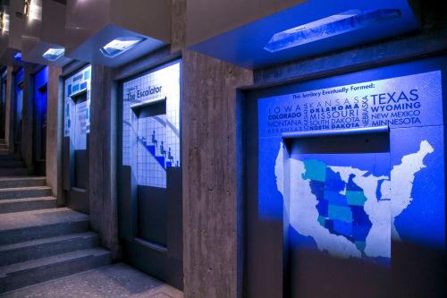 Illuminated wall displays featuring maps and text about U.S. territories and states, with a staircase in the background.