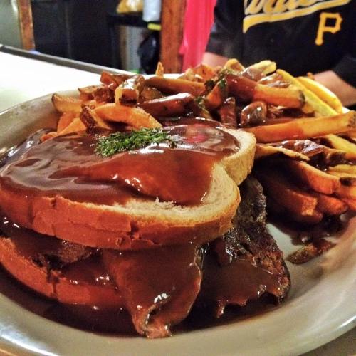 A plate featuring a sandwich with meat and gravy, served with a side of crispy French fries.