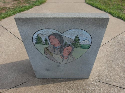 A stone monument featuring a heart-shaped illustration of two Indigenous figures against a natural background.
