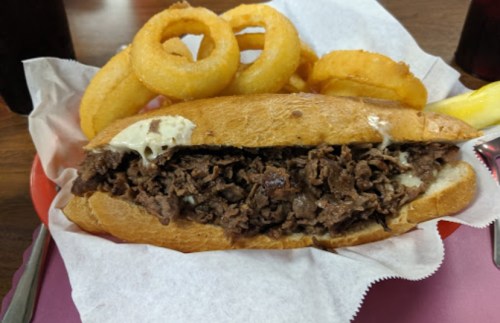 A hearty sandwich filled with shredded beef, served with onion rings and a pickle on the side.