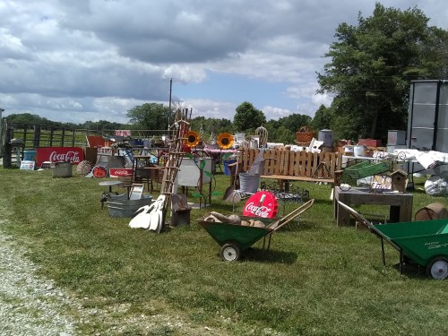 A variety of vintage items and decorations displayed outdoors, including signs, furniture, and garden tools on a grassy area.