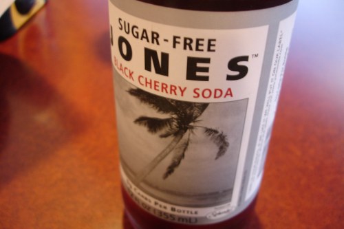 A close-up of a Jones Black Cherry Soda bottle with a palm tree graphic on the label.