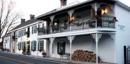 Historic building with white exterior, decorative balcony, and festive holiday decorations along the porch and windows.