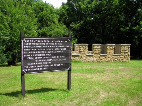 A stone wall ruins beside a sign with text about its history, set in a green, wooded area.