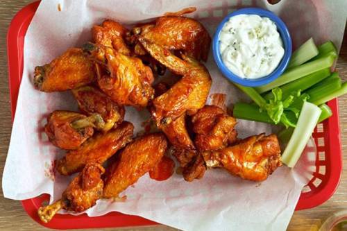 A basket of crispy chicken wings with a side of celery and blue cheese dressing.